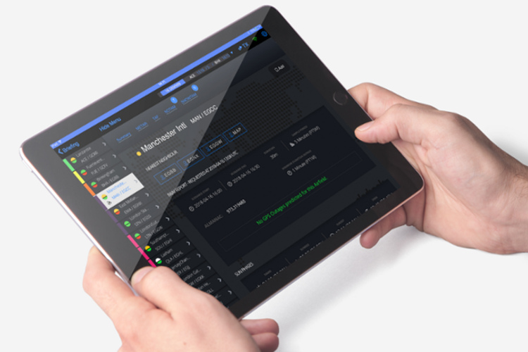 A tablet is held in a pair of hands. The screen displays crew briefing information. 