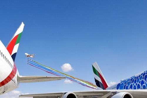 The image from Dubai Airshow 2019 two aircraft on the runway with five aircraft in the air with colourful plumes of smoke coming from the engines.